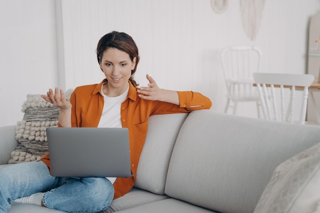 Überraschtes Mädchen, das per Videoanruf am Laptop chattet, erstaunt über gute Nachrichten, die zu Hause auf der Couch sitzen