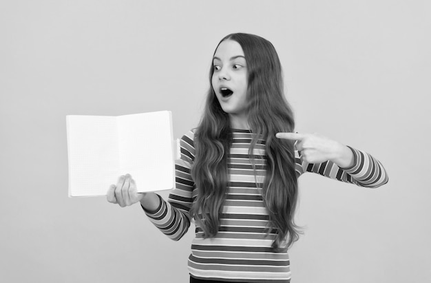 Überraschtes Mädchen zeigt mit dem Finger auf offenes Buch, um den gelben Hintergrund zu kopieren