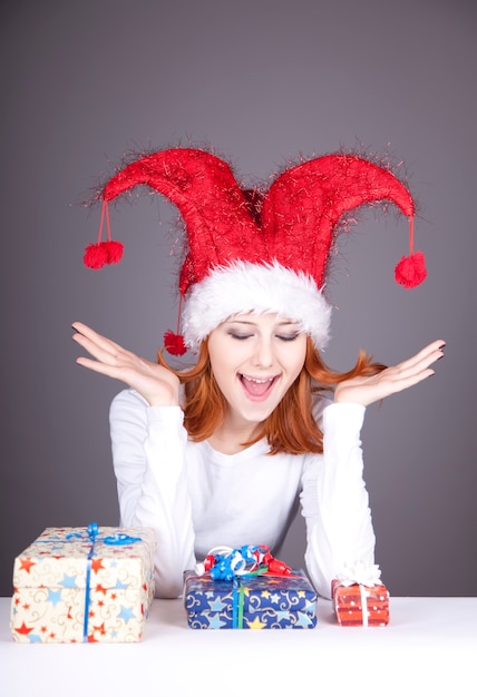 Überraschtes rothaariges Mädchen in der Weihnachtsmütze mit Geschenkboxen.