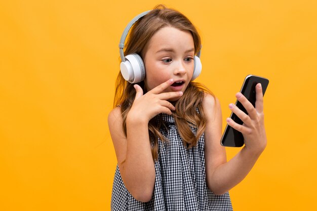 Überraschtes Schulmädchen betrachtet ein Smartphone auf einem gelben Hintergrund