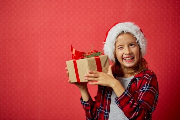 Überraschtes und positives kleines Mädchen in Weihnachtsmütze mit Weihnachtsgeschenk