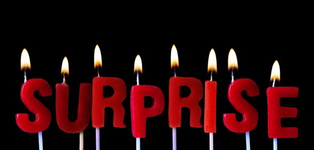 Überraschung in roten Geburtstagskerzen vor schwarzem Hintergrund