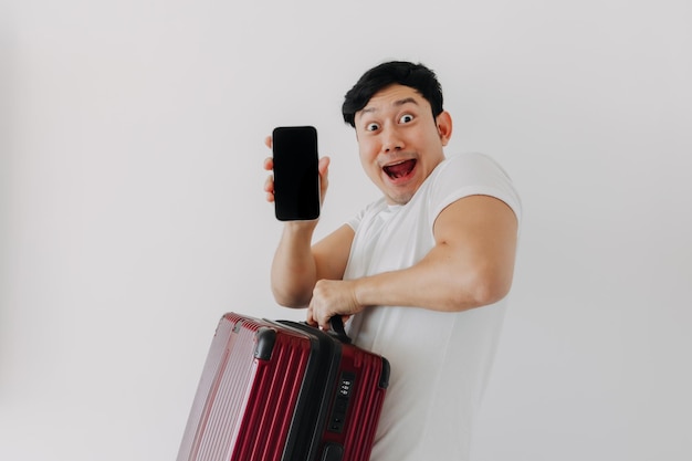 Überraschung und Wow-Gesicht eines asiatischen Mannes, der einen Koffer hochhält und die Handy-Anwendung zeigt
