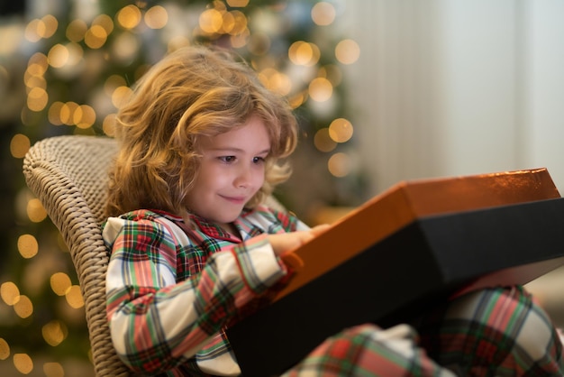 Überraschungskind eröffnet Weihnachtszauber und präsentiert glückliches Kind in der Nähe des Weihnachtsbaums zu Hause