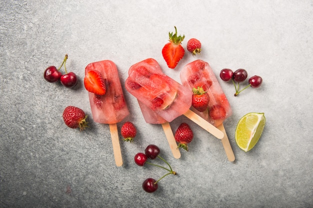 Berry Popsicle mit Holzstöcken auf Betontheke. Hausgemachte Erdbeer-gefrorene Fruchtriegel