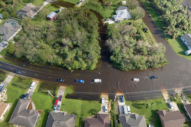 Überschwemmte amerikanische Straße mit beweglichen Fahrzeugen und umgeben von Wasserhäusern in einem Wohngebiet in Florida Folgen einer Hurrikan-Naturkatastrophe