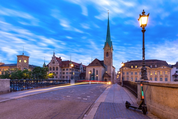 Berühmte Fraumünsterkirche und Münsterbrücke über die Limmat während der abendlichen blauen Stunde in der Altstadt von Zürich, der größten Stadt der Schweiz