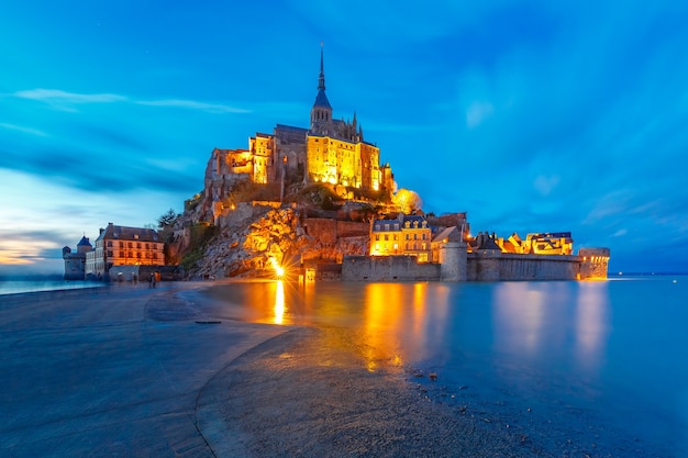 Berühmter Mont Saint Michel beleuchtet in der blauen Abendstunde mit Reflexion bei Flut, Normandie, Frankreich