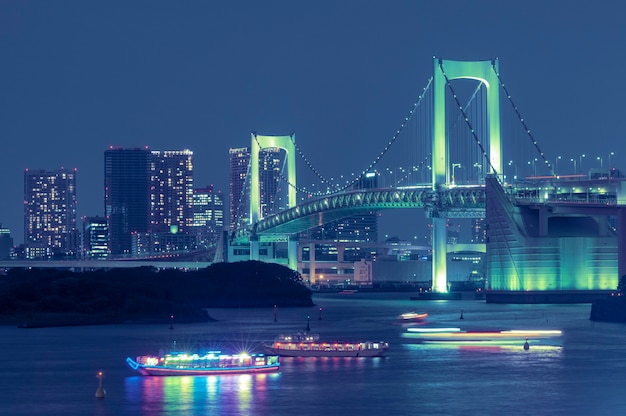 Berühmtes Wahrzeichen, die Tokyo Rainbow Bridge über dem Buchtwasser mit malerischer Nachtbeleuchtung und traditionellen japanischen Booten