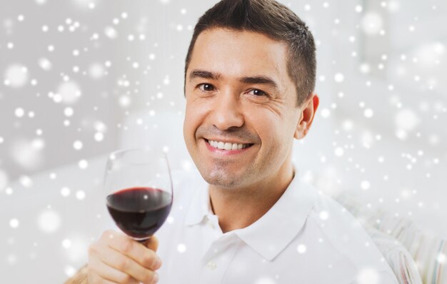 beruf, getränke, freizeit, urlaub und personenkonzept - glücklicher mann, der rotwein aus glas über schneeeffekt trinkt