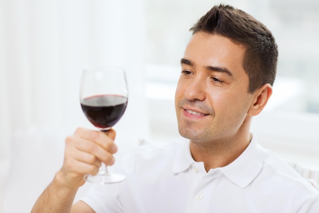 beruf, getränke, freizeit, urlaub und personenkonzept - glücklicher mann, der zu hause rotwein aus glas trinkt