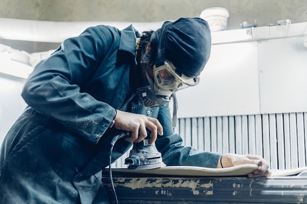 Beruf, Menschen, Tischlerei, Emotion und Menschenkonzept - Ein Tischler schneidet ein Brett mit einer elektrischen Stichsäge. Herstellung von Skateboards. er hat schutzkleidung und maske.