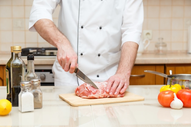 Berufskoch, der messer hält und fleisch schneidet.