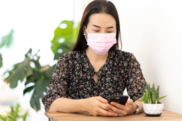 Berufstätige Frauen tragen Gesichtsmaske mit Smartphone Sitzen zu Hause arbeiten