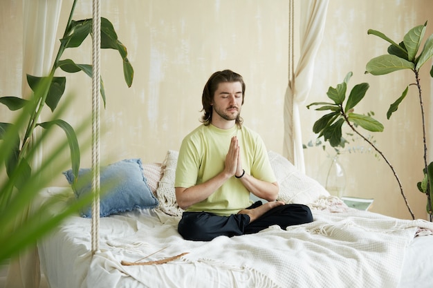 Beruhigter Mann in Yoga Sana auf dem Bett und Namaste, friedliche Meditation Teacer konzentriert sich am Morgen zu Hause