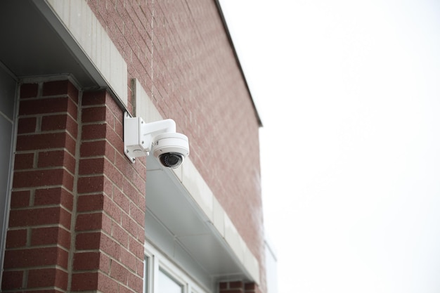 Überwachungskamera, die an einem Gebäude mit Blick auf eine belebte Straße montiert ist, während die Kamera am Straßenrand an einer Mastkappe angebracht ist