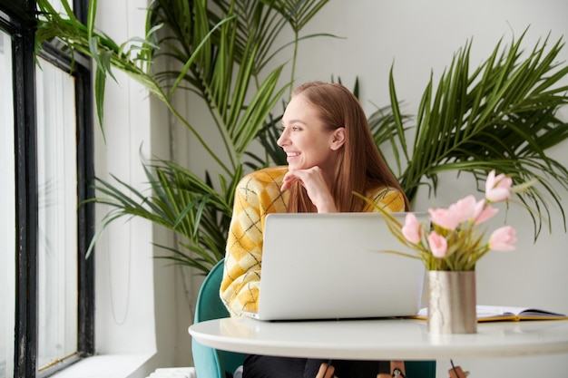 Überzeugte junge Frau in der intelligenten Freizeitkleidung, die an Laptop arbeitet