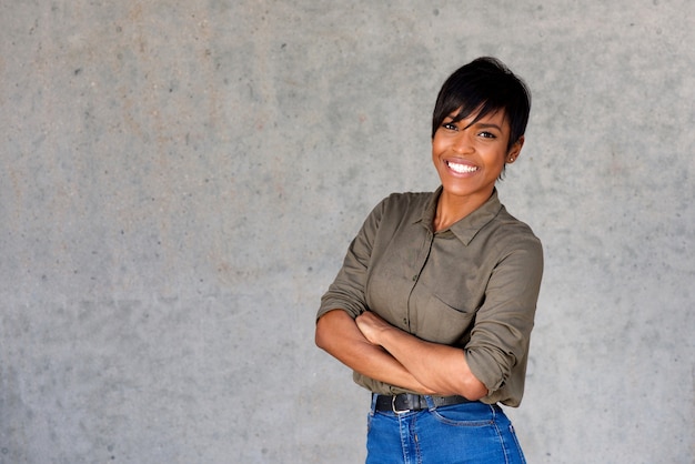Überzeugte junge schwarze Frau, die gegen graue Wand lächelt