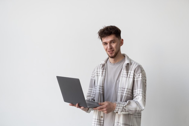 Überzeugter Geschäftsexperte Überzeugter junger gutaussehender Mann, der Laptop hält und bei der Stellung gegen weißen Hintergrund lächelt