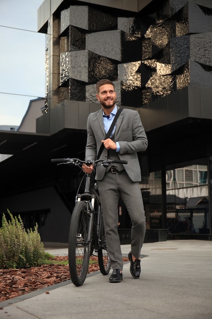 Überzeugter junger Geschäftsmann, der mit dem Fahrrad auf der Straße in der Stadt geht.