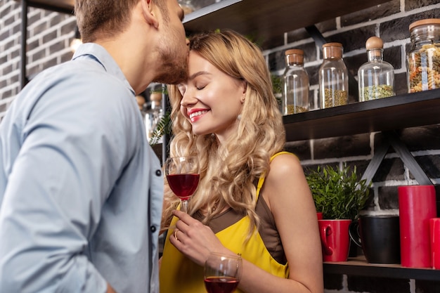 Besando la frente. Radiante novia rubia atractiva sonriendo mientras su hombre besa su frente