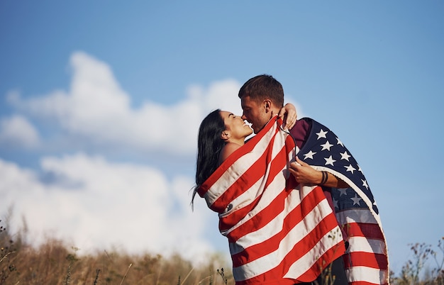 Besándose. Siente la libertad. Hermosa pareja con bandera americana pasar un buen rato al aire libre en el campo.