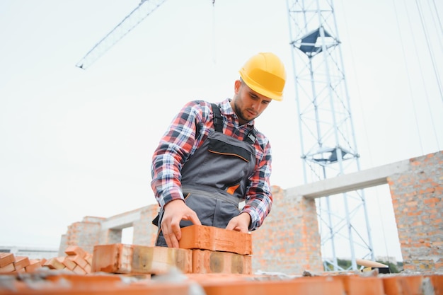 Beschäftigt mit Ziegelmauer Bauarbeiter in Uniform und Sicherheitsausrüstung haben Arbeit am Bau