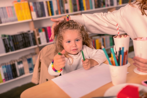 Beschäftigt sein. Freundliches Baby, das Ellbogen auf Tisch lehnt, während man Bild zeichnet