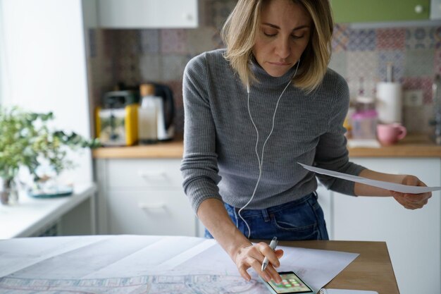 Beschäftigte Architektin arbeitet an Bauplan-Check-Entwurf mit Bauplan auf digitalem Tablet von zu Hause aus