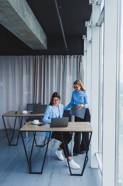 Beschäftigte Geschäftsfrauen mit einem Laptop im Büro, die sich Inhalte auf dem Laptop ansehen und das Projekt gemeinsam besprechen, während sie während einer Arbeitspause im Büro sitzen Teamwork-Unternehmensdiskussion