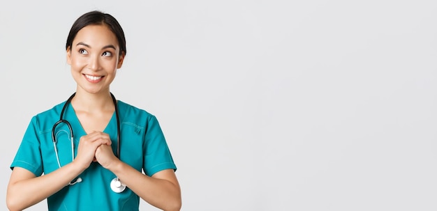 Beschäftigte im Gesundheitswesen, Virusprävention, Konzept der Quarantänekampagne. Entschlossene und selbstbewusste asiatische Ärztin in Scrubs, ballen die Hände zusammen, machen sich fertig und schauen in die obere linke Ecke