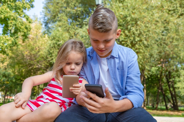 Beschäftigte kinder, die ihre telefone betrachten, die sms simsen und draußen sitzen spielen