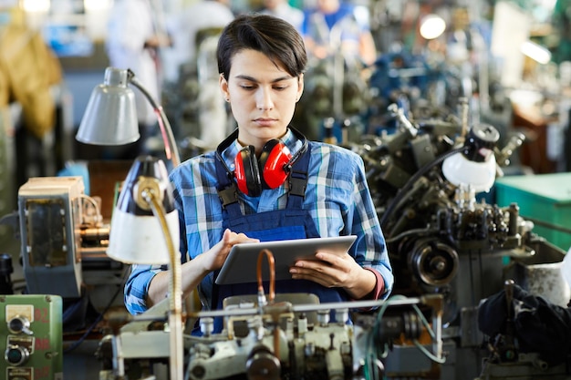 Beschäftigter Fabrikangestellter synchronisiert Tablet mit moderner Maschine