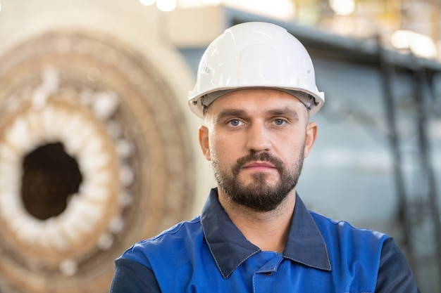 Beschäftigter junger Fabrikarbeiter in Overalls, der die Arbeitsdatei auf dem Tablet überprüft, während er in der Industrie arbeitet