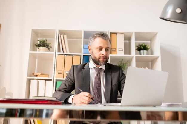 Beschäftigter Mann im Anzug, der Informationen auf Laptop analysiert