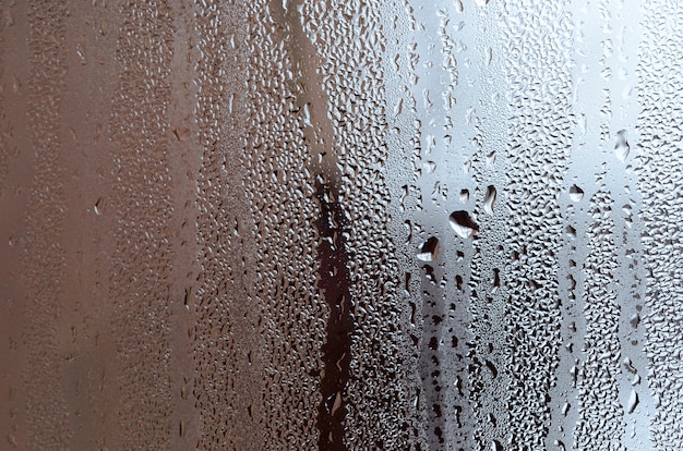 Beschaffenheit eines Tropfens des Regens auf einem nassen transparenten Glashintergrund. Grau getönt
