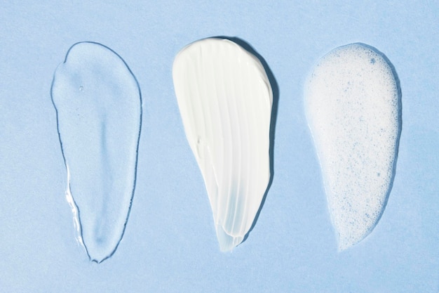 Beschaffenheiten einiger kosmetischer Produkte auf einem weißen Körpercremeschaum des blauen Hintergrundes Draufsicht