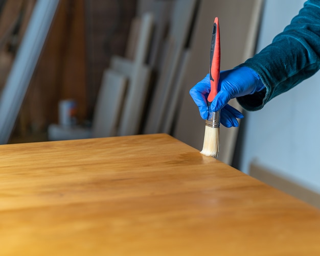 Beschichtung der Holzoberfläche mit Schutzlack. Hand in blauen Gummihandschuh verwendet Pinsel. Speicherplatz kopieren