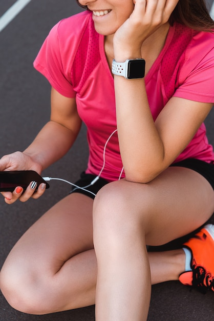 beschnittene Ansicht der glücklichen Frau in der Smartwatch, die Smartphone mit leerem Bildschirm auf Laufbahn hält