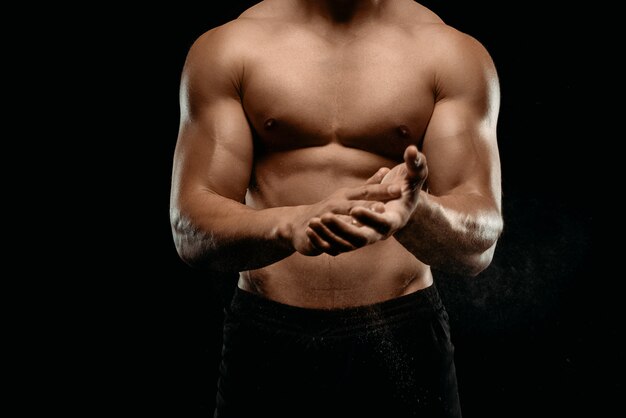 Beschnittene Ansicht des sportlichen Bodybuilders mit dem muskulösen Torso, der Talk auf den auf Schwarz lokalisierten Händen anwendet