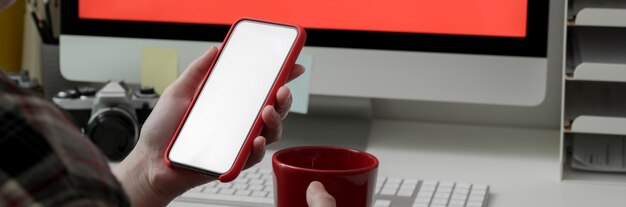 Beschnittene Aufnahme der Freiberuflerin mit Smartphone mit leerem Bildschirm und Kaffeetrinken