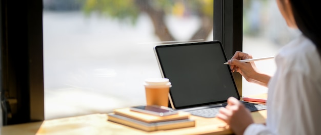 Beschnittene Aufnahme der jungen Studentin, die sich auf ihre Aufgabe mit Tablette, Kaffeetasse und Briefpapier konzentriert