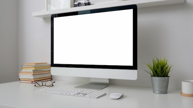 Beschnittene Aufnahme des Arbeitsbereichs mit Computer mit leerem Bildschirm, Büchern und Dekorationen auf weißem Schreibtisch