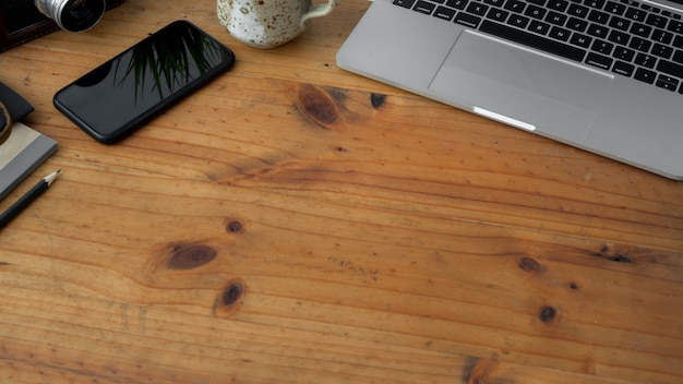 Beschnittene Aufnahme des Arbeitsbereichs mit Laptop, Teetasse, Smartphone und Kopierraum auf rustikalem Holzschreibtisch
