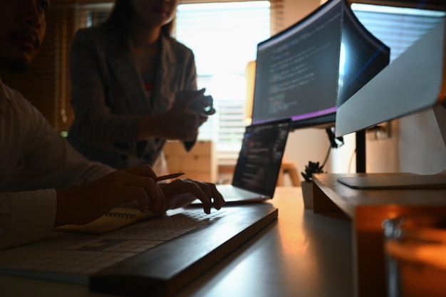 Foto beschnittene aufnahme von entwicklern, die in einem dunklen büro brainstorming-programmiercode auf einem computerbildschirm durchführen