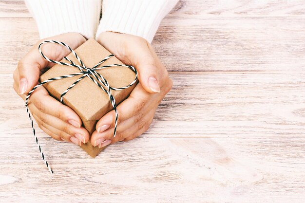 Foto beschnittene hände halten ein geschenk auf dem tisch