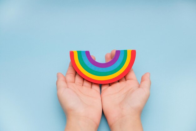 Foto beschnittene hände halten einen künstlichen regenbogen über blauem hintergrund