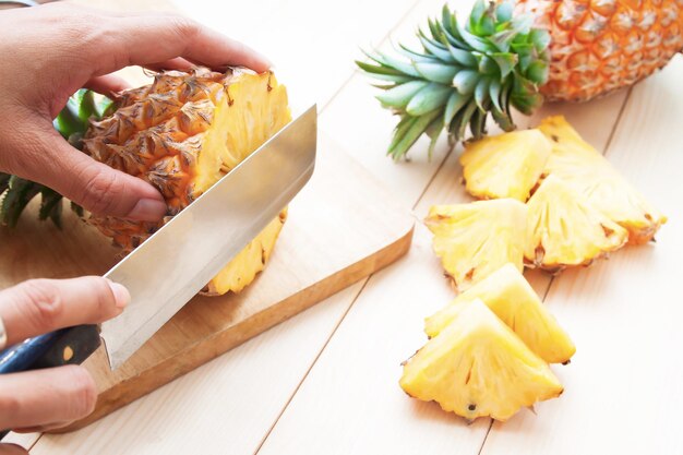 Foto beschnittene hände schneiden ananas auf dem tisch