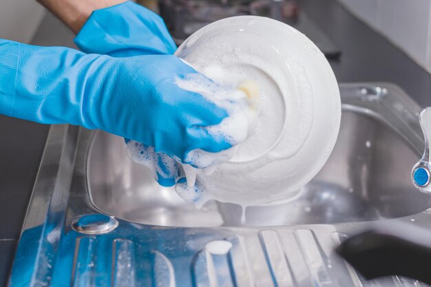 Foto beschnittene hände tragen handschuhe und waschen geschirr im waschbecken