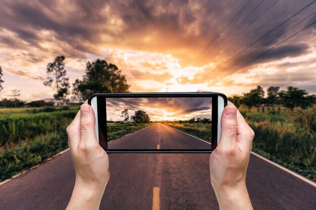 Beschnittene Hand einer Person, die während des Sonnenuntergangs mit einem Handy gegen den Himmel fotografiert